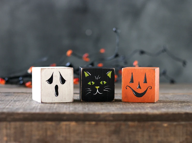 Three building blocks style sitters, painted to look like a ghost, a black cat and a pumpkin.